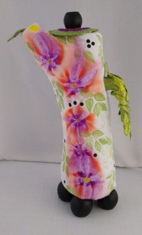 Pitcher made from an arm cast, painted quilt, air dry clay, wooden bottle tops, part of a belt buckle, and drawer handle.