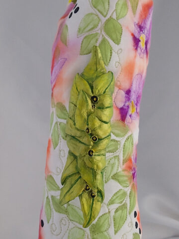 Pitcher made from an arm cast, painted quilt, air dry clay, wooden bottle tops, part of a belt buckle, and drawer handle.